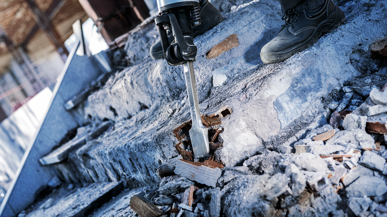 PRO HEX-4C Spade Chisel 28 mm, 80 x 400 mm A person wearing safety equipment uses a demolition hammer to break concrete stairs.