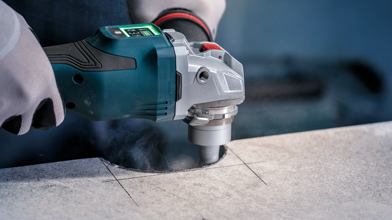 Person wearing safety equipment drills a circular hole into a stone slab.