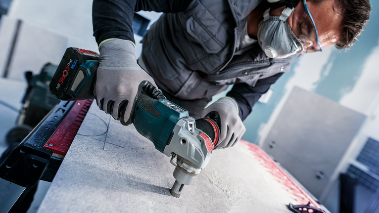 Person wearing safety equipment drills into a stone slab on a workbench.