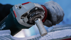 Person wearing safety equipment grinds a stone surface with a rotary power tool.