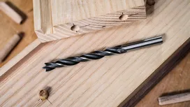 Twist drill bit lying on wooden planks in a carpentry workspace.