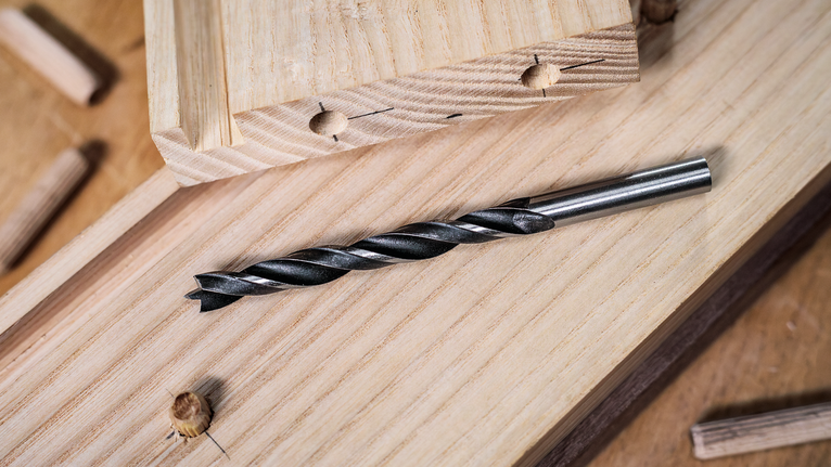 Twist drill bit lying on wooden planks in a carpentry workspace.
