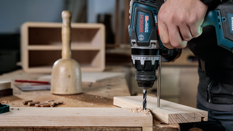 Person drills a hole into wooden planks in a workshop.