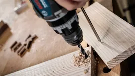 Person drills a hole into wooden boards in a workshop.
