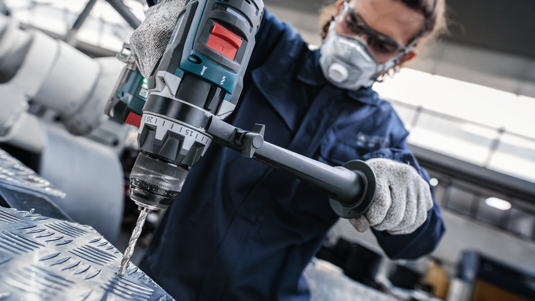 PRO Metal HSS-G Hex Twist Drill Bit Set, 5 pcs Person wearing safety equipment drills into a metal sheet in an industrial workshop.