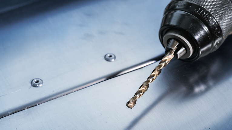 PRO Stainless Steel HSS-Co Twist Drill Bit Set, 19 pcs Electric drill with a metal drill bit resting on a steel sheet.