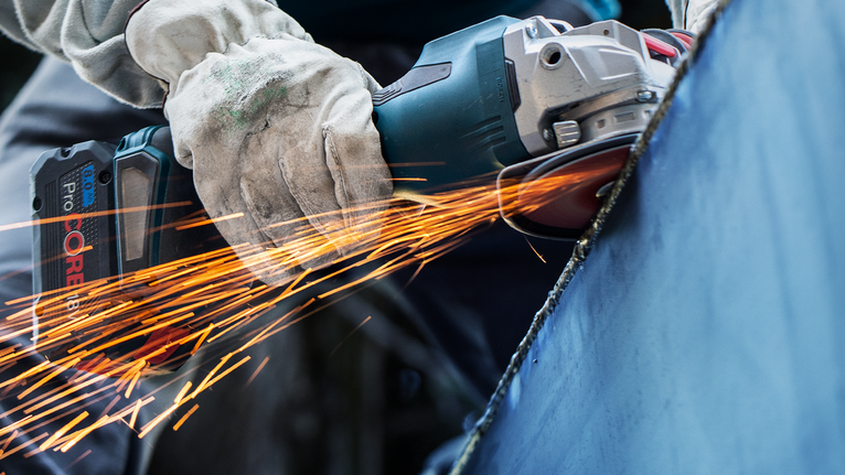 PRO Backing Pad Soft, 125 mm, M14 A person wearing safety equipment grinds metal, creating a shower of sparks.