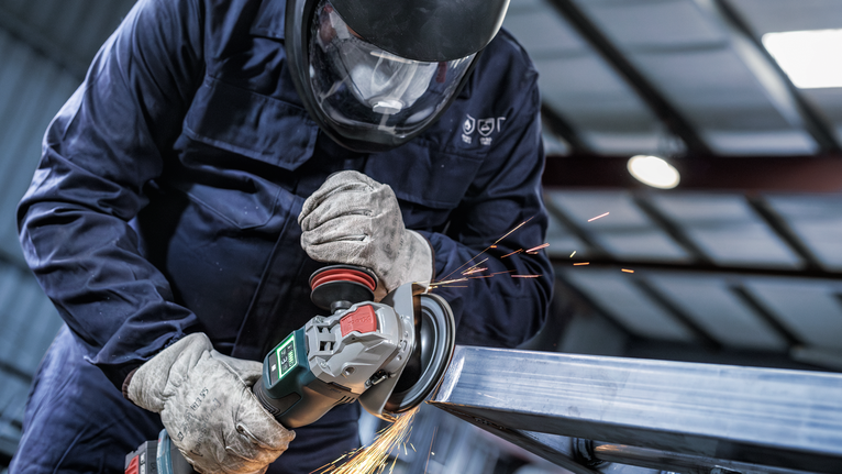 PRO Backing Pad Clip, X-Lock A person wearing safety equipment grinds metal, creating sparks.