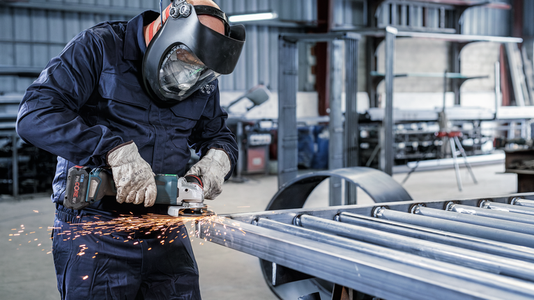 PRO Backing Pad Clip, X-Lock A person wearing safety equipment grinds metal, creating sparks.