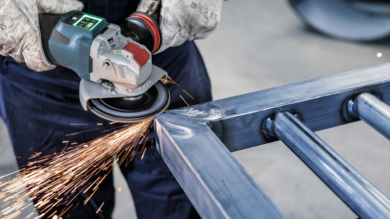 PRO Backing Pad Clip, X-Lock Person wearing safety equipment grinds metal, producing bright sparks.