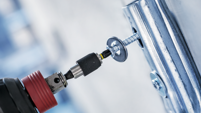 Cordless drill driving a screw into a metal frame.