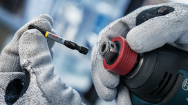 Person wearing safety equipment changes a drill bit on a power tool.