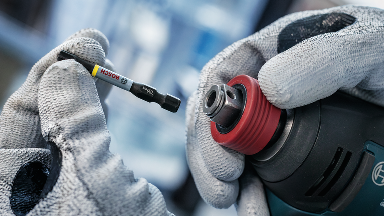 Person wearing safety equipment changes a drill bit on a power tool.