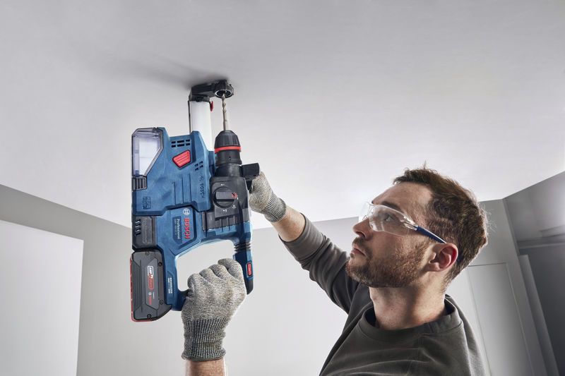 GBH 18V-22 X A person wearing safety equipment drills into a ceiling using a cordless rotary hammer.