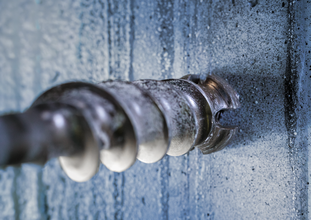 Metal drill bit boring into a concrete wall.