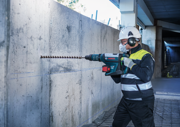 Object #200479698: 3065448_app_web_007 Person wearing safety equipment drills into a concrete wall with a rotary hammer.