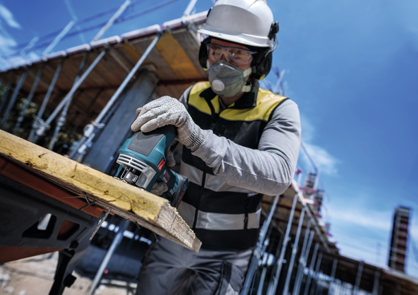 Person wearing safety equipment cuts wood with a jigsaw at a construction site.