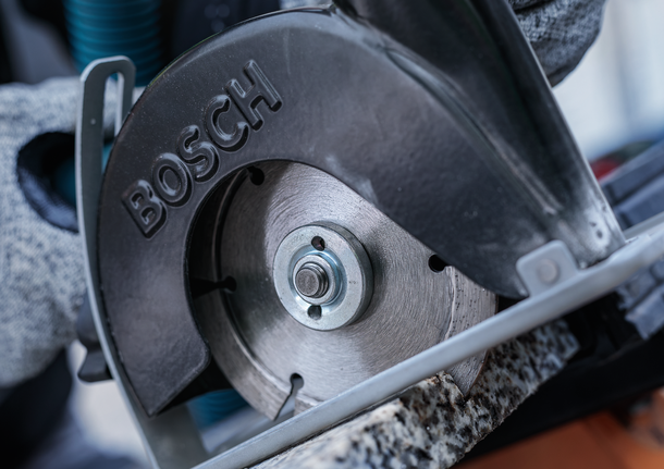 Person wearing safety equipment cuts stone with a circular saw.