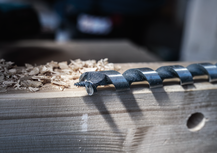 Large auger drill bit resting on a wooden plank with wood shavings beside it.