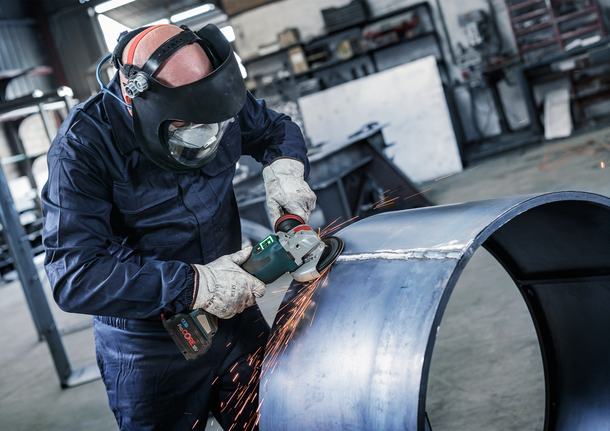 PRO Backing Pad Clip, X-Lock Person wearing safety equipment grinds the edge of a large metal pipe, producing sparks.