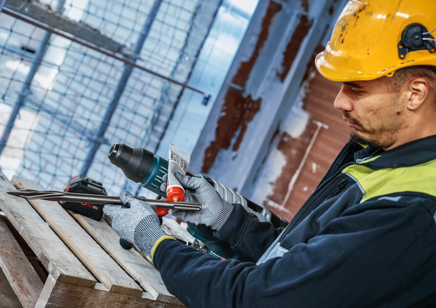 PRO SDS Shank Grease, for Drill and Chisel Person wearing safety equipment applies lubricant to a drill attachment on a construction site.