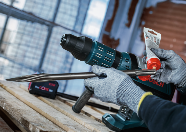 PRO SDS Shank Grease, for Drill and Chisel Person wearing safety equipment applies lubricant to a metal drill bit indoors.
