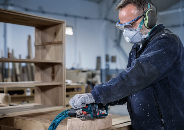 Person wearing safety equipment sands a wooden board in a workshop.