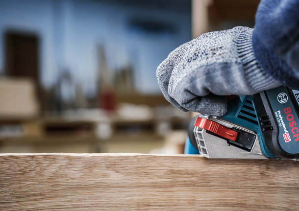 Person wearing safety equipment uses a power planer on a wooden board.