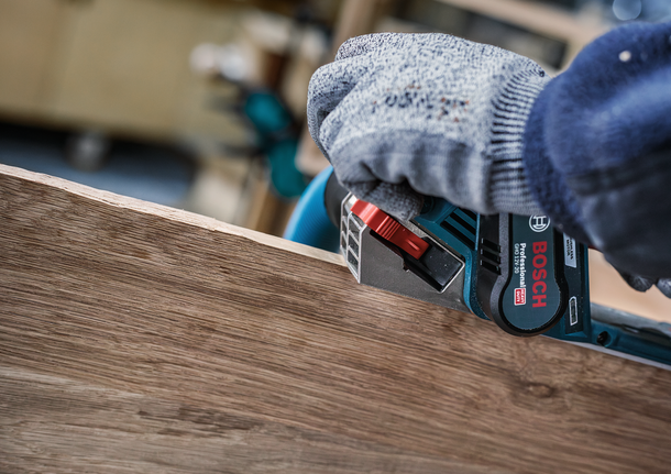Person wearing safety equipment smooths the edge of a wooden board with a power tool.
