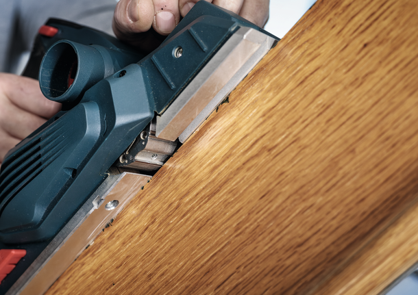 Person uses a power planer to smooth the edge of a wooden board.