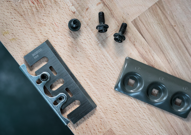 Metal blade, fastening screws, and a mounting plate arranged on a wooden surface.
