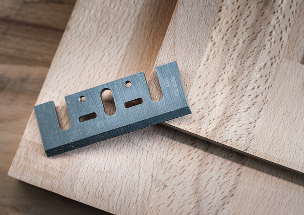 Metal cutter blade resting on a wooden board.