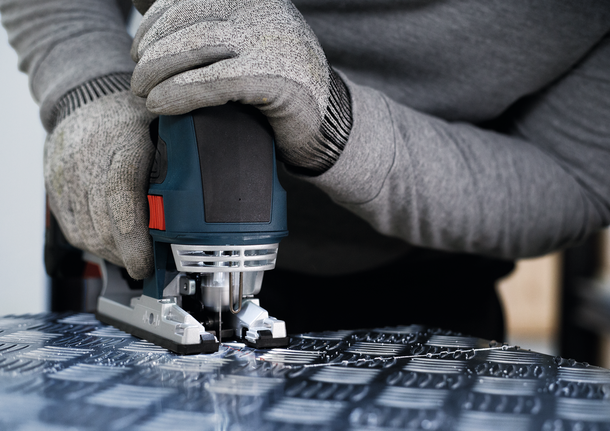 PRO Alu T127D Jigsaw Blade, 100 mm, 5 pcs Person wearing safety equipment uses a jigsaw to cut patterned metal.