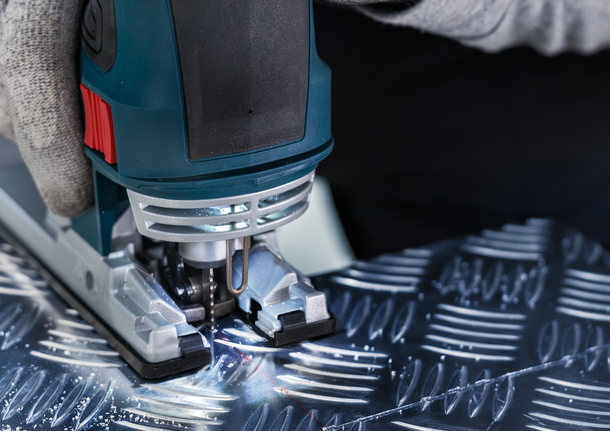 PRO Alu T127D Jigsaw Blade, 100 mm, 5 pcs A person wearing safety equipment uses a jigsaw to cut patterned metal.