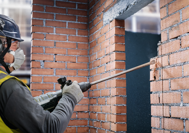 PRO SDS max-4C Flat Chisel, 25 x 600 mm Person wearing safety equipment chisels a brick wall with a demolition hammer.