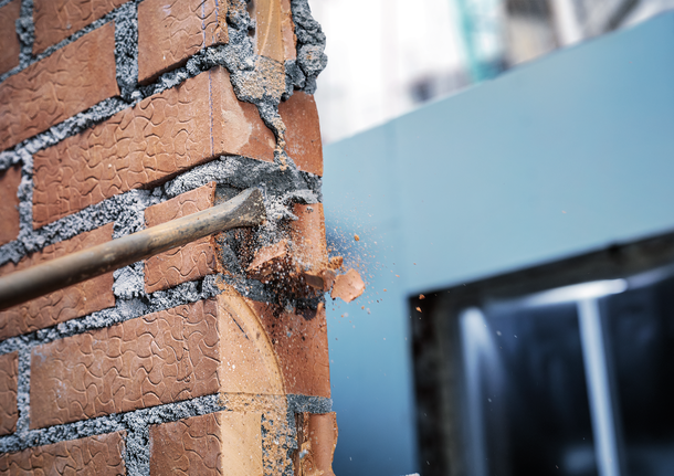 PRO SDS max-4C Flat Chisel, 25 x 600 mm Chisel breaking a brick wall, causing debris to scatter.