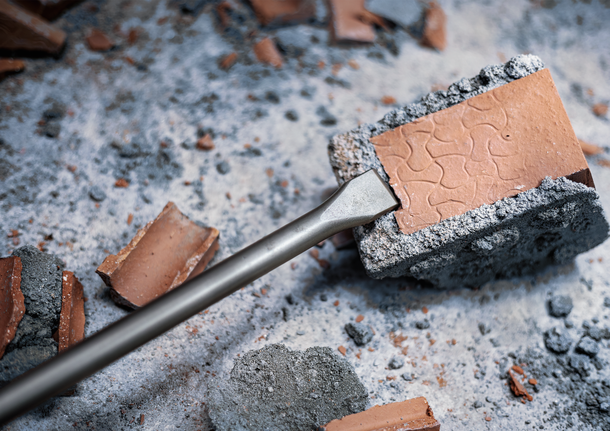 PRO SDS max-4C Flat Chisel, 25 x 600 mm Chisel breaking a brick on a dusty construction surface.
