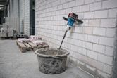 Cordless stirring tool mixes material in a bucket at a construction site.