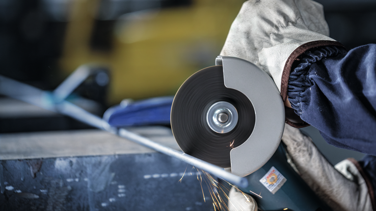 PRO Metal Cutting Disc, 100 x 2.5 x 16 mm Person wearing safety equipment cuts metal pipe using an angle grinder.