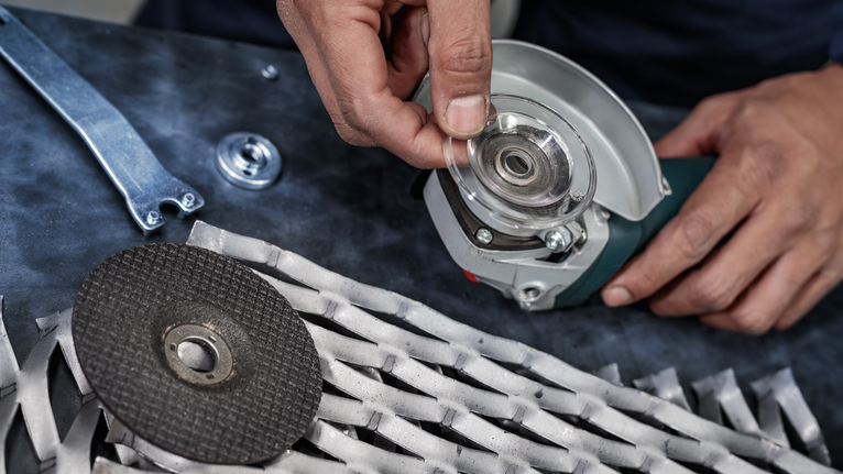 Person assembling a cutting disc onto a grinder near metal mesh on a workbench.