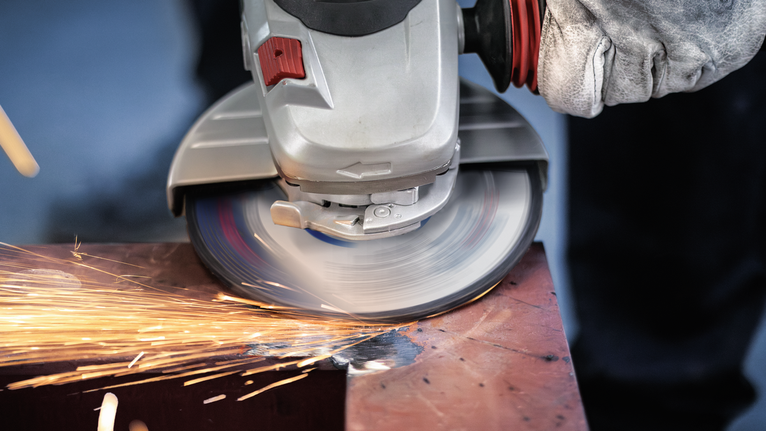 PRO Metal Grinding Disc, A 24 S BF, 180 x 6.6 x 22.23 mm, Depressed Centre Person wearing safety equipment grinds metal using an angle grinder, creating sparks.