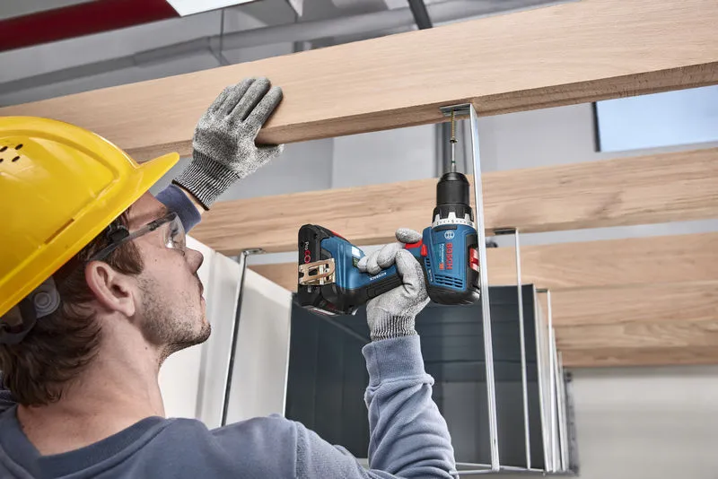 GSR 18V-65 A person wearing safety equipment uses a cordless drill to fasten a screw into a wooden beam.