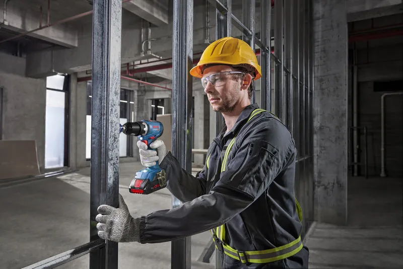 A person wearing safety equipment uses a cordless drill on a metal frame.