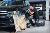 A person wearing safety equipment polishes a car door with a cordless polisher.
