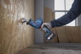 A person wearing safety equipment uses a reciprocating saw to cut plywood.