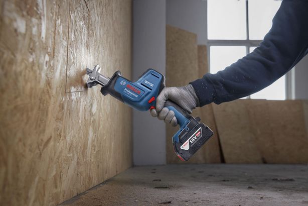 A person wearing safety equipment uses a reciprocating saw to cut plywood.