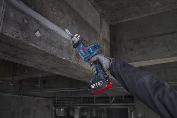A person wearing safety equipment uses a reciprocating saw to cut metal overhead.