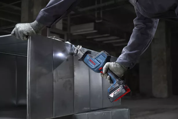 A person wearing safety equipment cuts sheet metal with a cordless reciprocating saw.