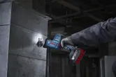A person wearing safety equipment cuts sheet metal with a cordless reciprocating saw.