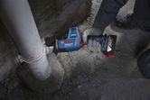 A person wearing safety equipment cuts a plastic pipe with a reciprocating saw.